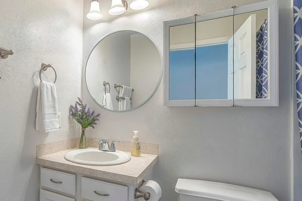 Modern bathroom vanity with round mirror, white cabinetry, and bright lighting