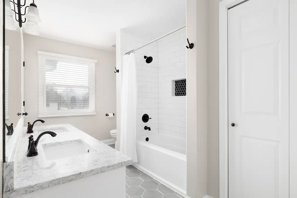 Modern bathroom with marble vanity countertop and white tiled shower with black fixtures