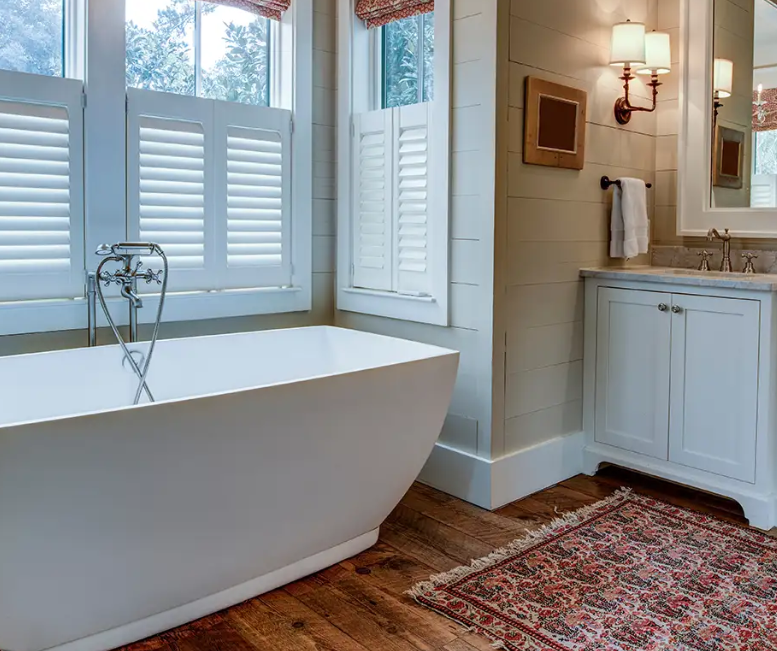 Luxury spa-style bathroom with freestanding soaking tub, wood flooring, and bright windows