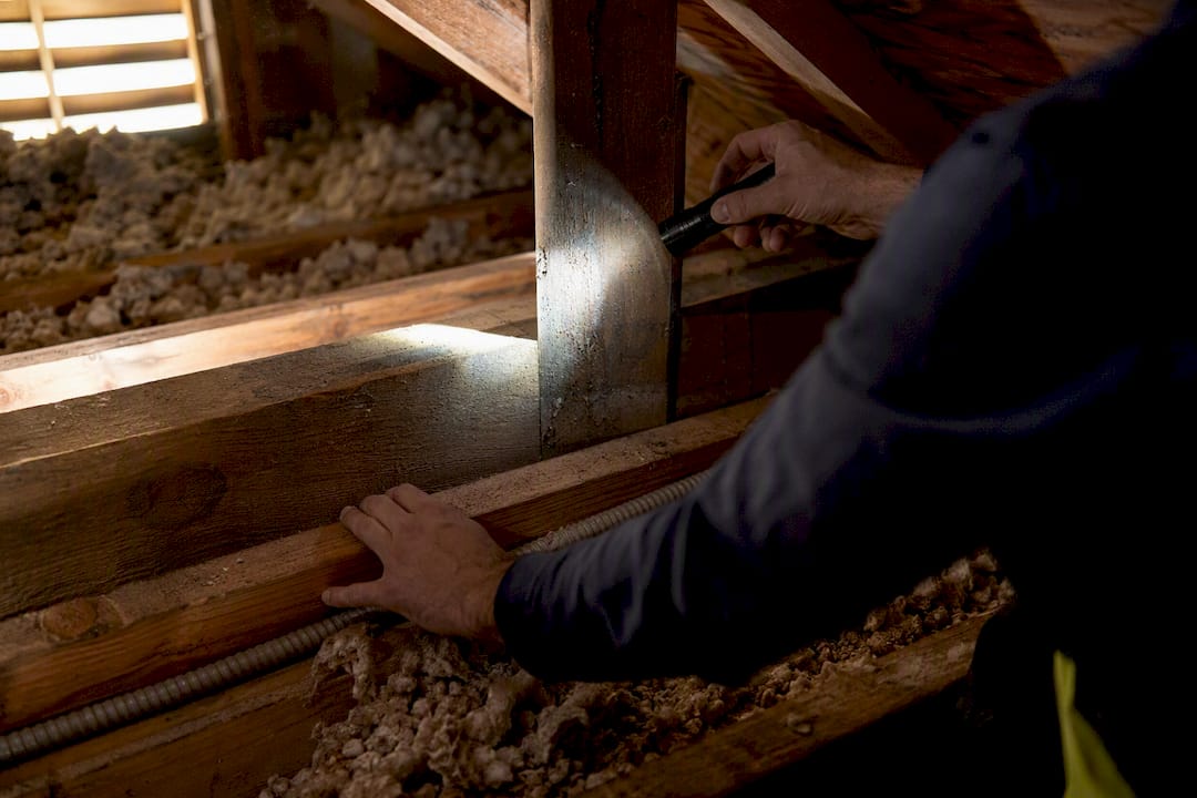 Inspector flashlight illuminating attic joists and beam